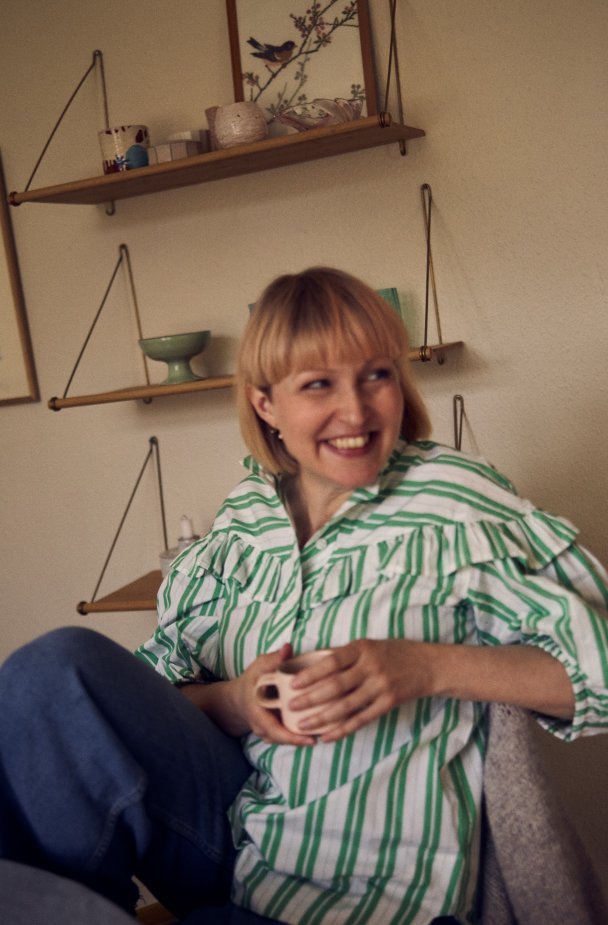 Pia Elgaard sidder på en stol i sin lejlighed og smiler med en kaffekop mellem hænderne