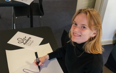 Nina Gantriis-Møller tegner. Ved siden af tegnepapiret ligger et print af designbyen Koldings nye logo, som Nina har skabt.