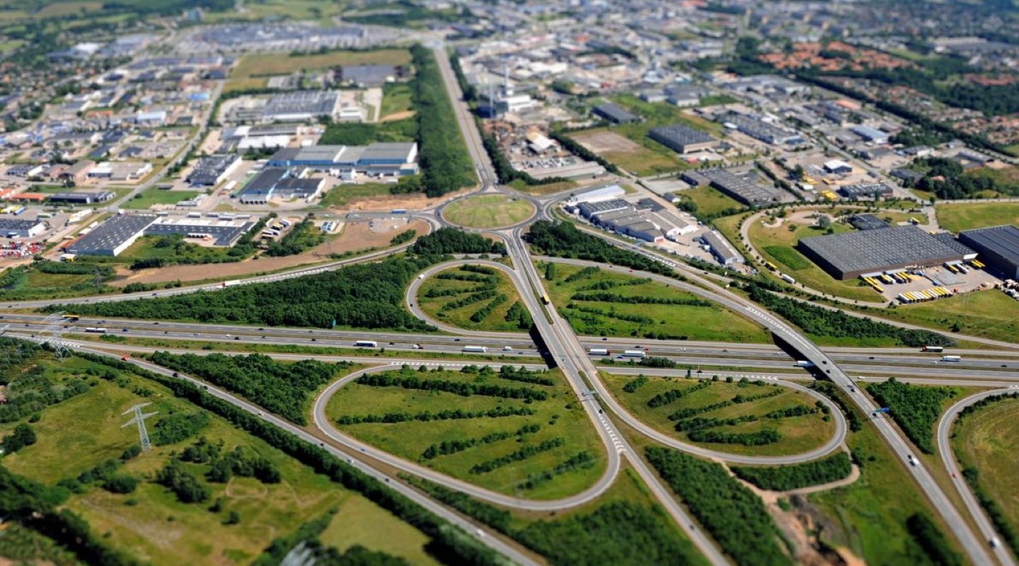 Dronefoto af motorvejskryds ved Kolding forrest i billedet med det tilgrænsende industriområde bagest i billedet