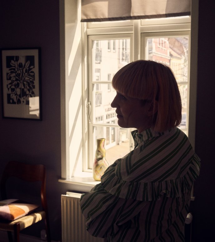 Pia Elgaard står i sin ældre lejlighed i midtbyen i Kolding og danner en silhuet i lyset fra et vindue
