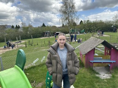 Lea står på en legeplads ved en daginstitution i Kolding. Hun står forrest i billedet. Børnene leger i baggrunden.