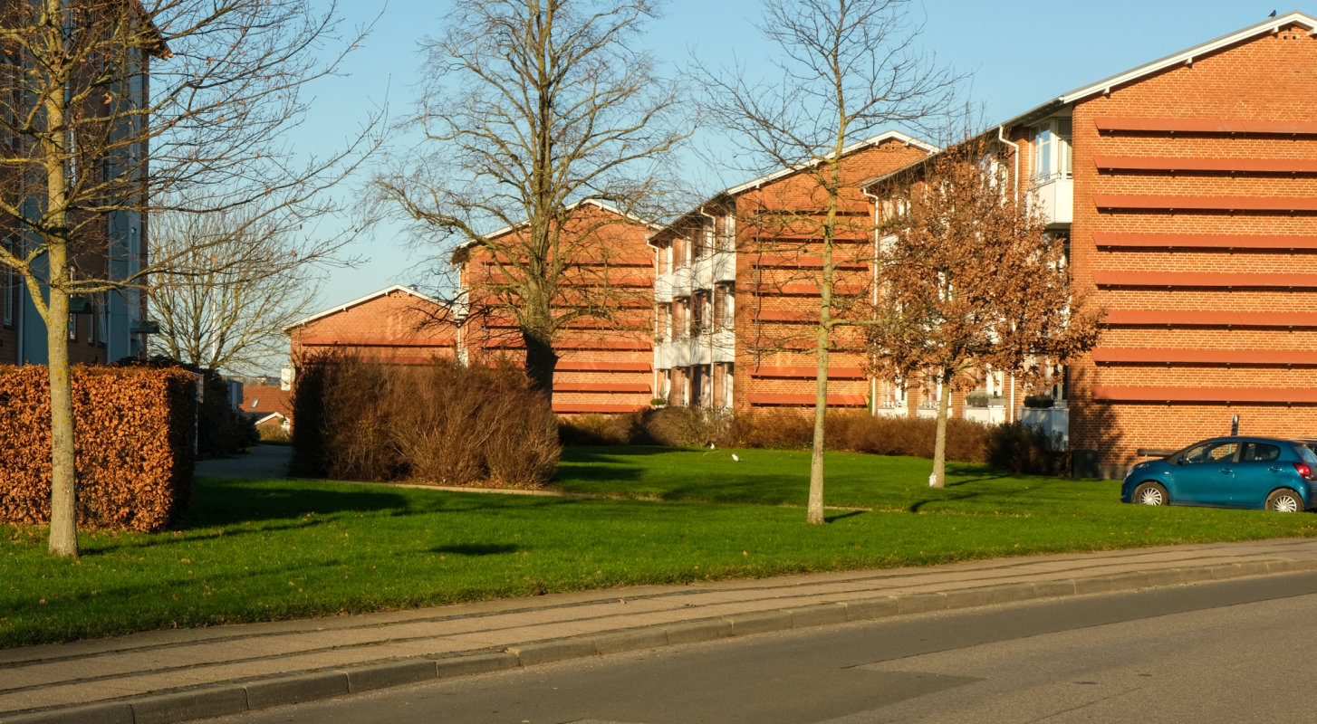 En stribe på 4 røde boligblokke med hvide altaner i Brændkjær-kvarteret i Kolding med grøn græsplæne, træer og hække