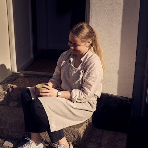 Maria Grønborg sidder på sin trappesten med forklæde på og med en kaffekop mellem hænderne