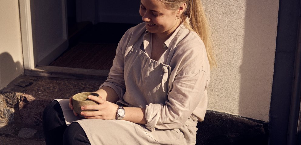 Maria Grønborg sidder på sin trappesten med forklæde på og med en kaffekop mellem hænderne