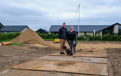 Thomas og Christina Graugaard-Nielsen står midt på deres byggegrund på Vesterengen i Viuf. Thomas står til venstre, Christina står til højre. Foran dem ligger deres hund Svend. Der er  bunker af jord på grunden