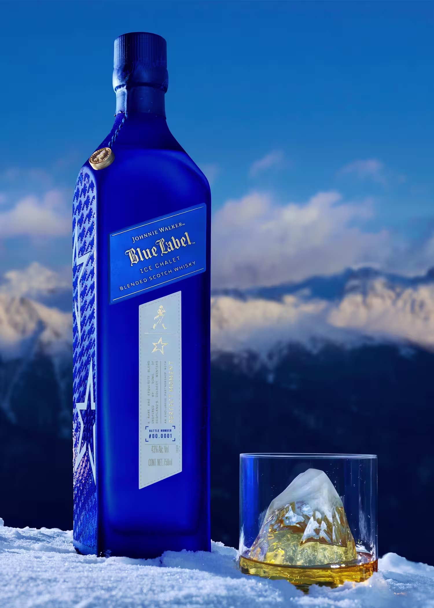 Johnnie Walker Blue Label Ice Chalet. A blue bottle of Johnnie Walker Blue Label Ice Edition whisky stands on snow next to a glass of whisky with a mountain-shaped ice cube, with snow-covered mountains in the background.