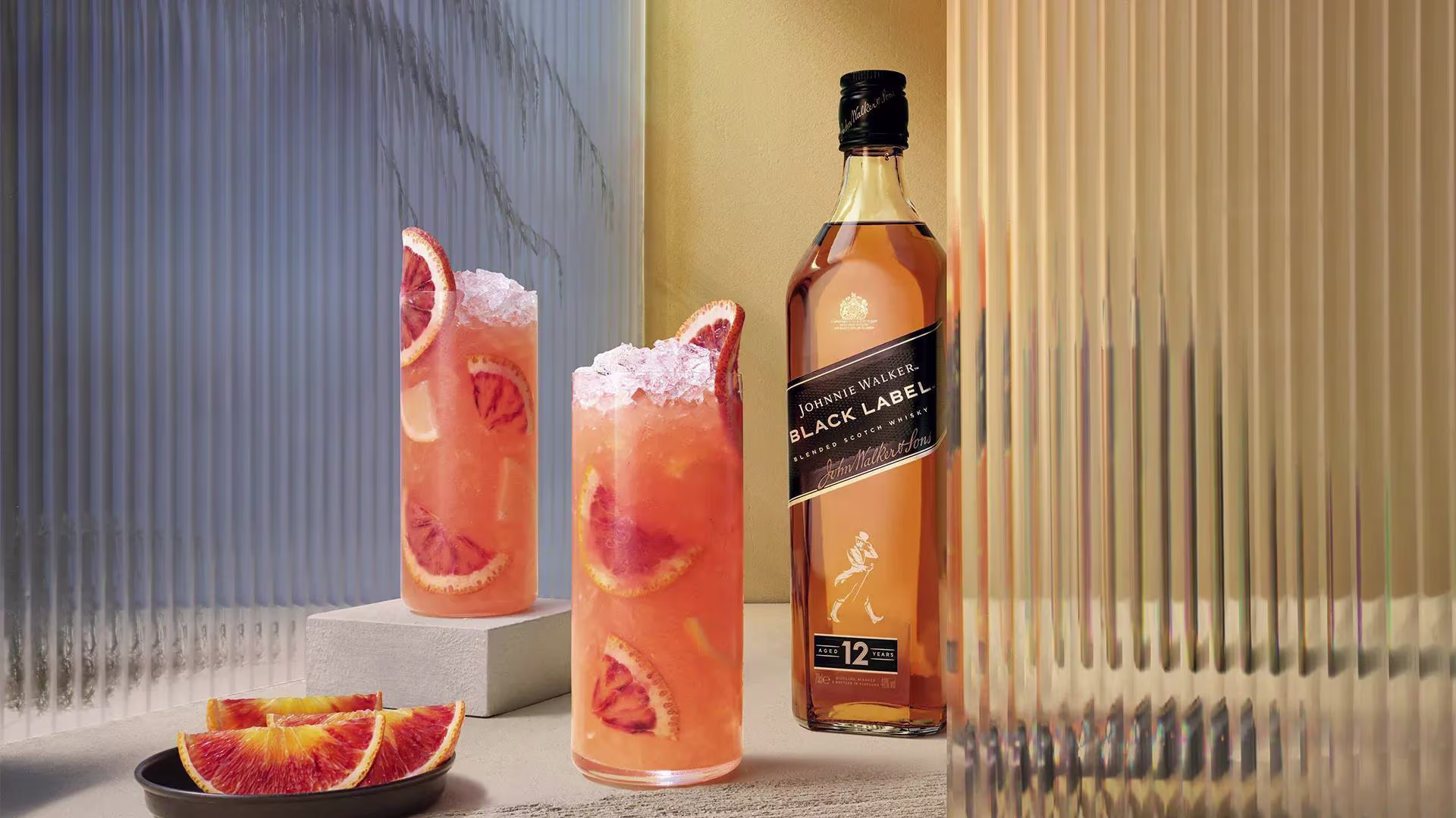 A hand garnishes a cocktail with an orange twist. Next to it stands a bottle of Black Label whisky. The scene is set against a vibrant orange background, emphasizing the golden hues of the whisky and drink.