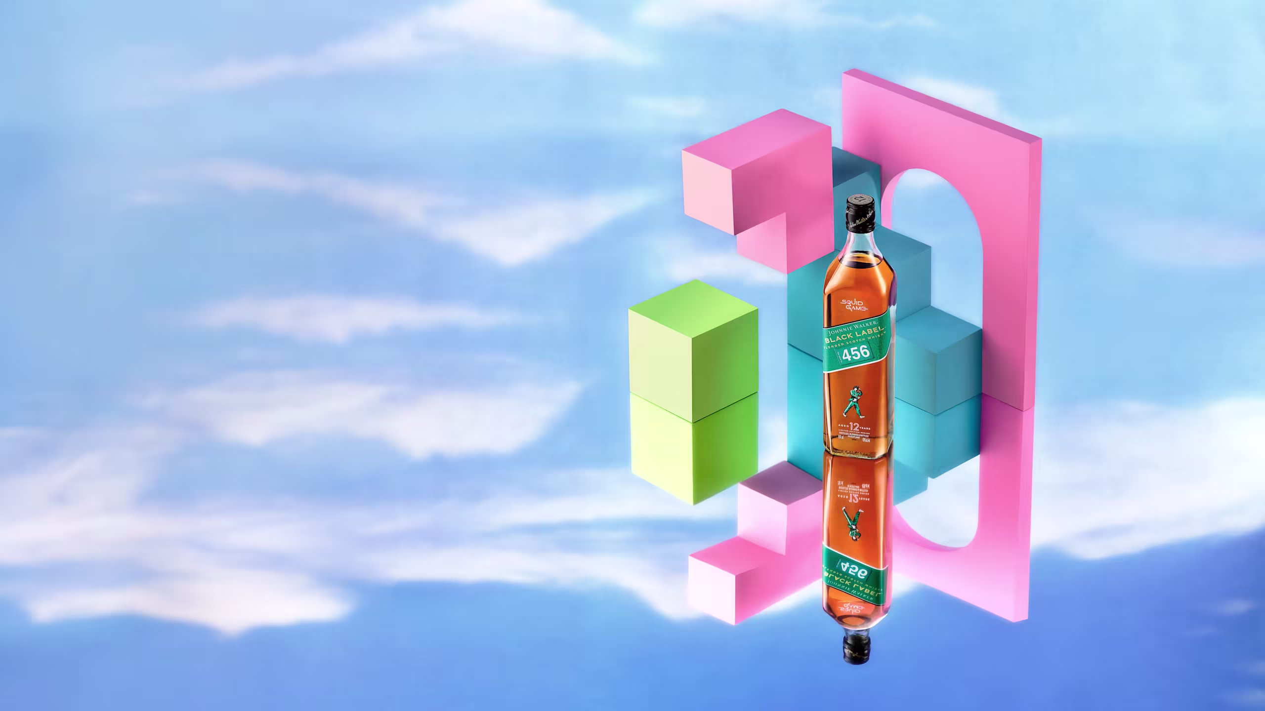 A bottle of Johnnie Walker Black Label 456 whiskey sits next to a tall glass with a light-colored drink and a slice of lemon. The background shows a bright blue sky with fluffy clouds.