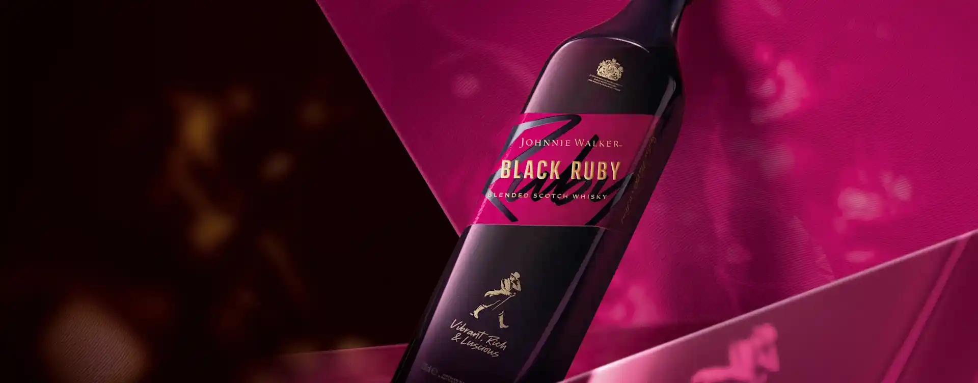 Una botella de Johnnie Walker Black Ruby se encuentra sobre un fondo rosa y oscuro. La etiqueta es oscura con letras doradas y presenta el icónico logotipo del hombre caminando.