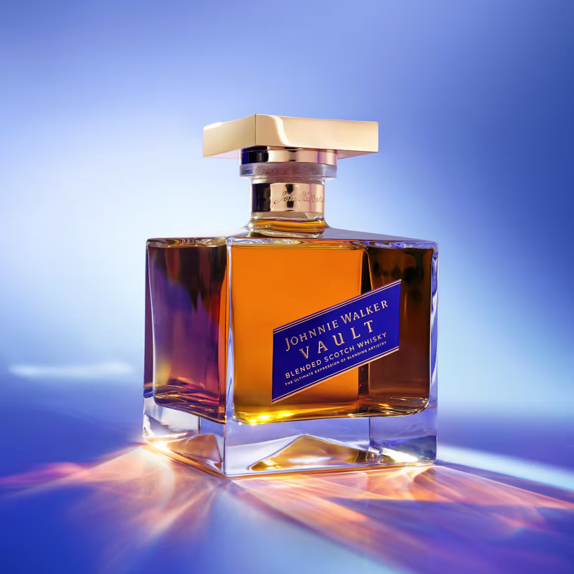 A bottle of Johnnie Walker Vault Blended Scotch Whisky on a reflective surface, lit in shades of blue and amber.