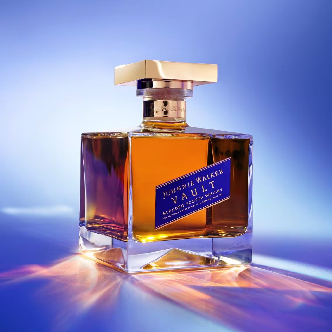A bottle of Johnnie Walker Vault Blended Scotch Whisky on a reflective surface, lit in shades of blue and amber.