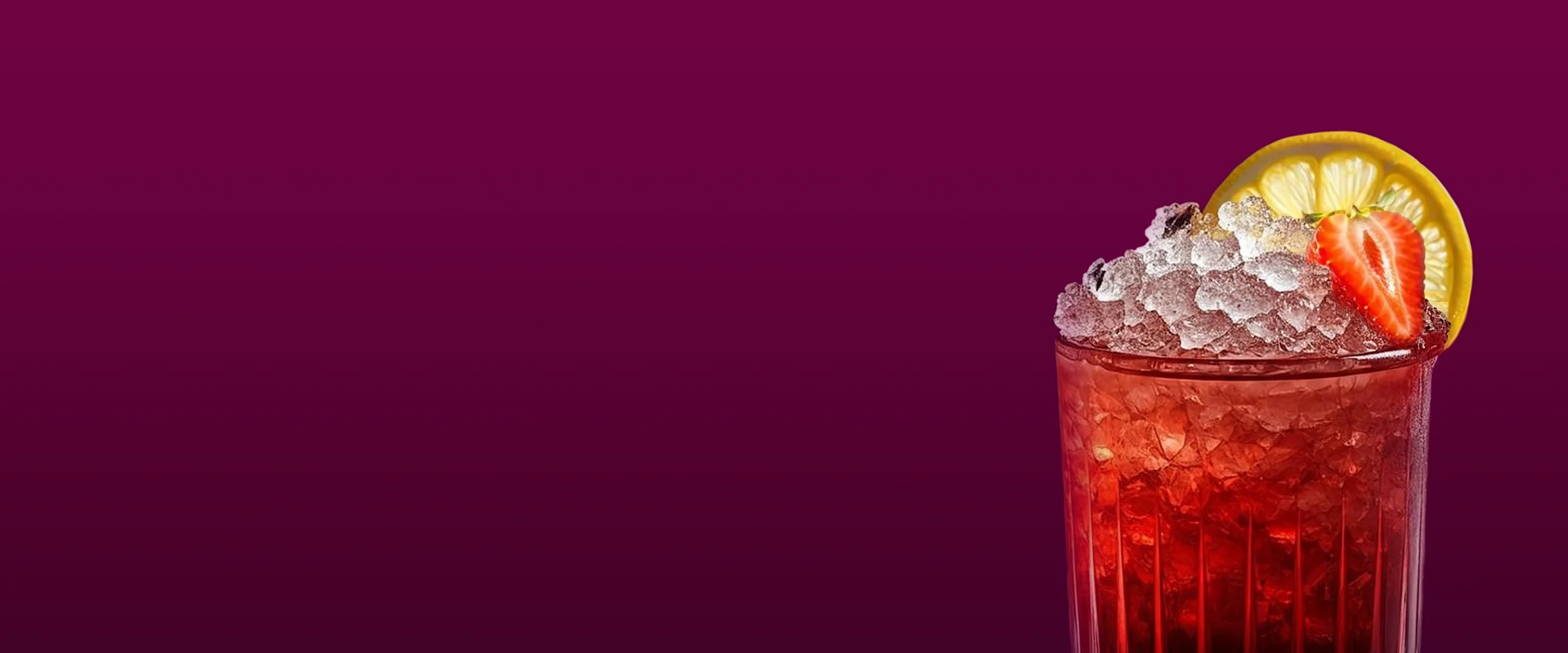 A glass filled with an ice-cold red drink, decorated with a lemon wedge and a strawberry, on a dark purple background.