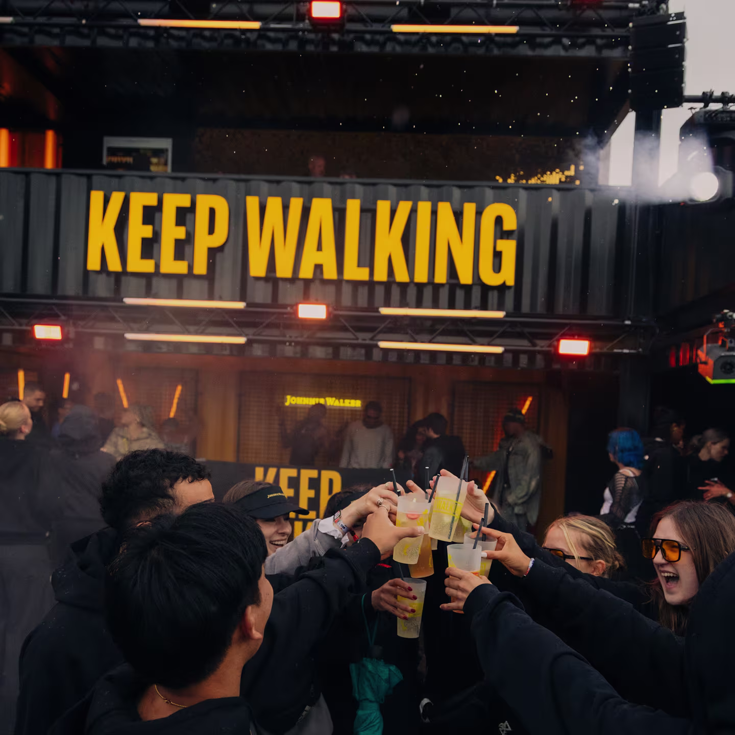Freunde stoßen vor einer Johnnie Walker Keep-Walking-Bar mit ihren Drinks an.