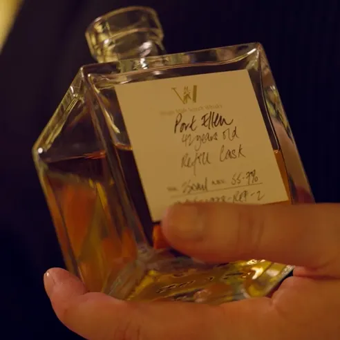 A person holding a square glass bottle of single malt scotch whiskey. The label reads Port Ellen, 42 years old, Refill Cask, with an alcohol volume of 55.7%. The background is slightly blurred.