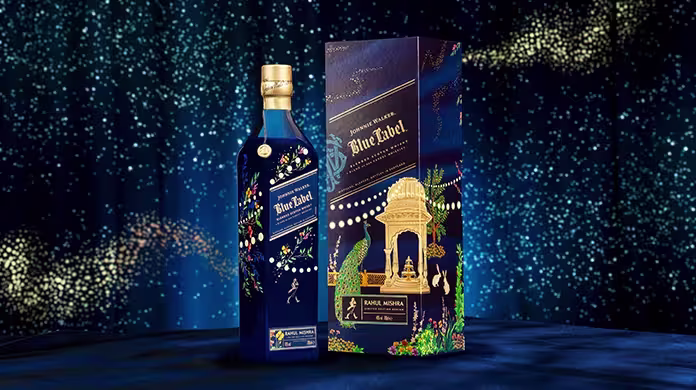 Butelka Johnnie Walker Blue Label w ozdobnym niebiesko-złotym pudełku z kwiatowymi wzorami i ozdobnym złotym łukiem, umieszczonym na ciemnoniebieskim tle z błyszczącymi efektami świetlnymi.