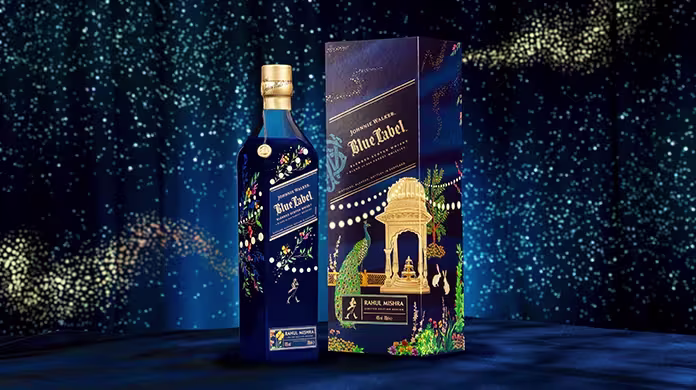 A bottle of Johnnie Walker Blue Label with a decorative blue and gold box featuring floral patterns and an ornate golden arch, set against a dark blue background with sparkling light effects.