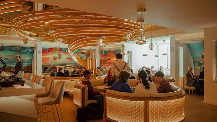  Um restaurante moderno e aconchegante, com grupos de pessoas jantando em mesas redondas. O teto apresenta uma impressionante instalação em espiral dourada, e murais coloridos decoram as paredes. Luminárias pendentes pendem sobre a área de estar.