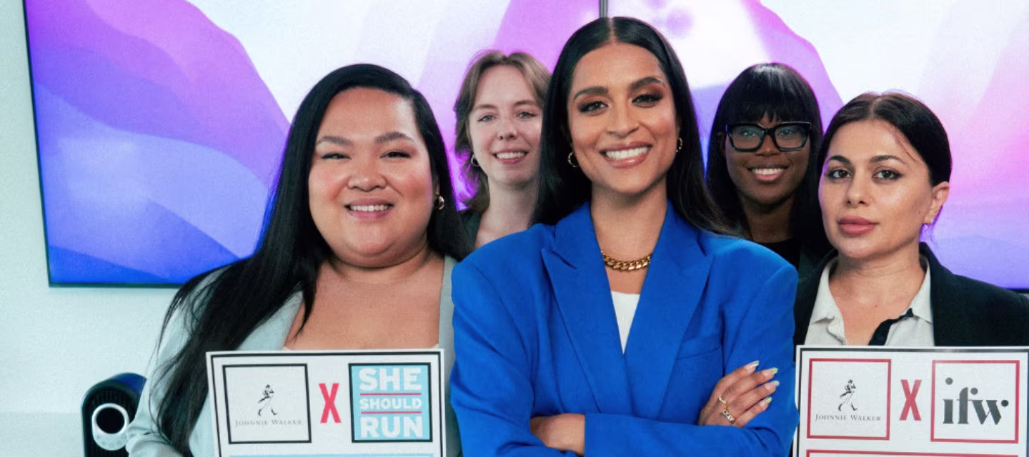 Five women stand together smiling, with two holding signs that say She Should Run and Xifw. The group appears confident and professional, against a colorful abstract background.