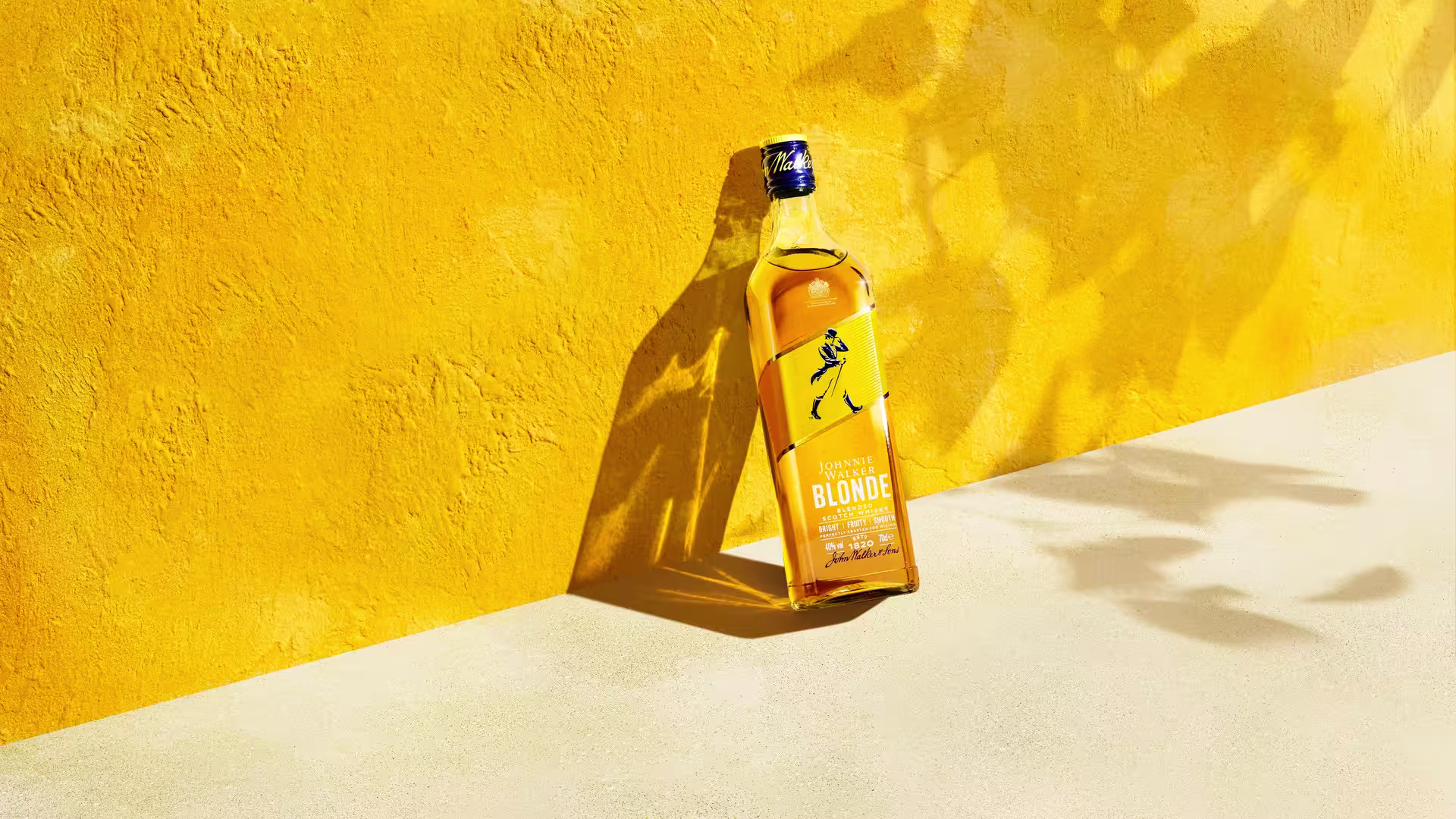 一瓶金色威士忌直立在充滿活力的黃色背景下,投下陰影。標籤上有一個藍色行走人物。陽光照射出紋理表面。