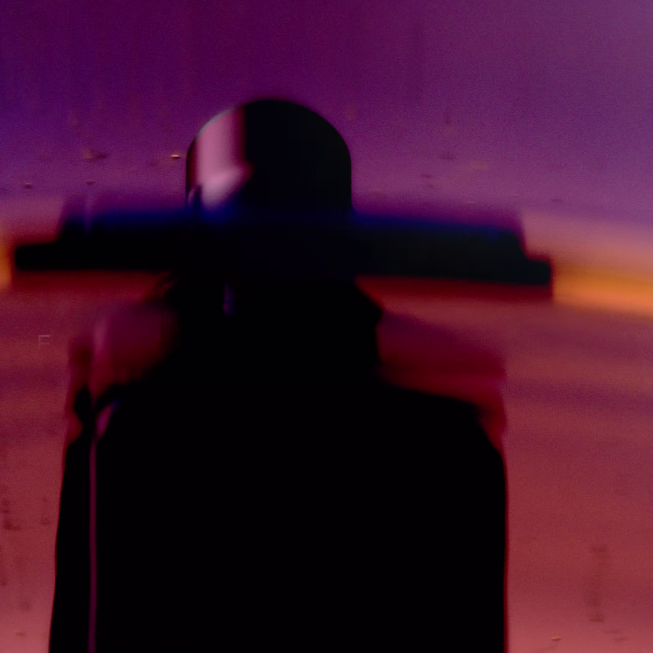 Blurred silhouette of a figure in a wide-brimmed hat against a purple and orange background.