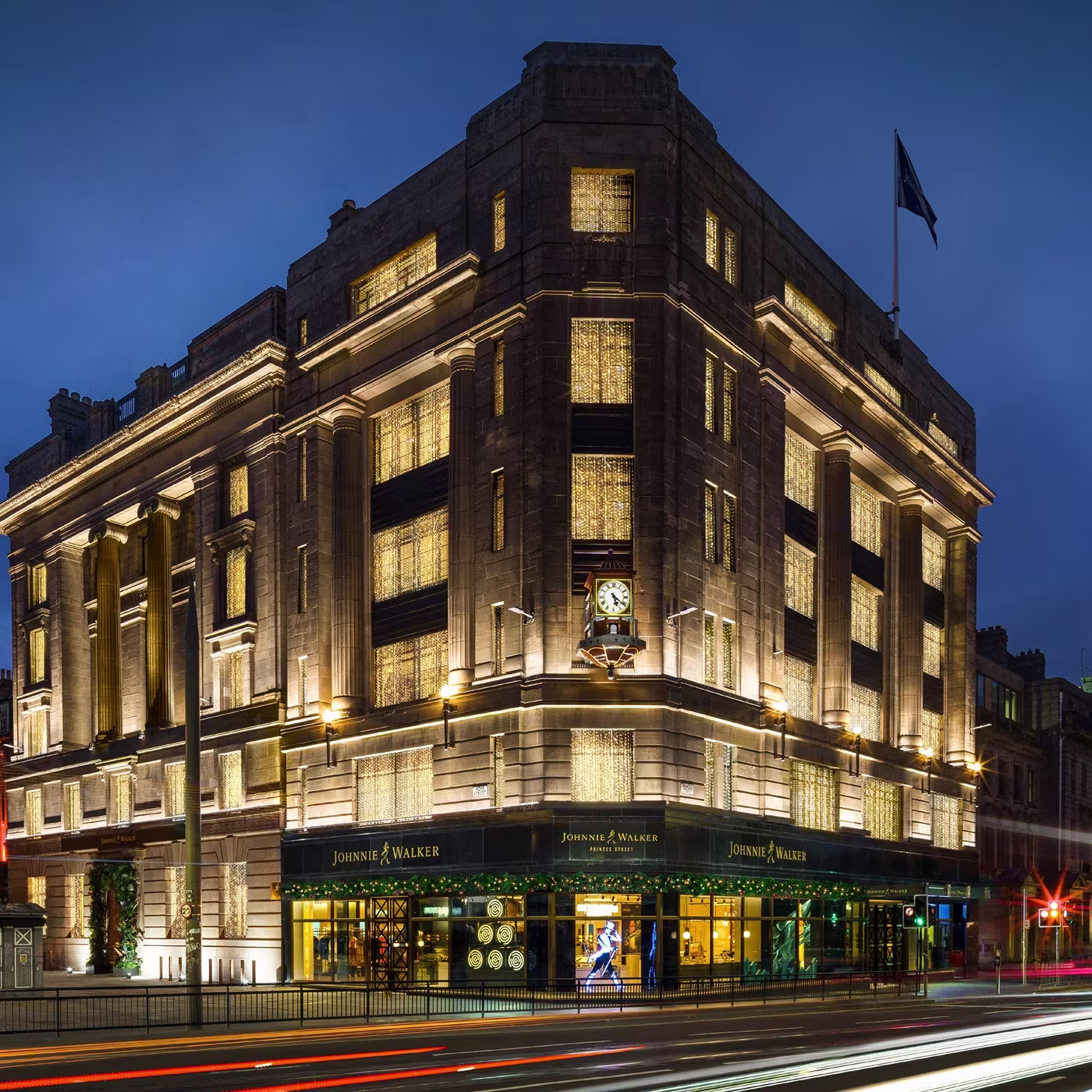 A brightly lit corner building at night with Johnnie Walker signage and a clock above the entrance.