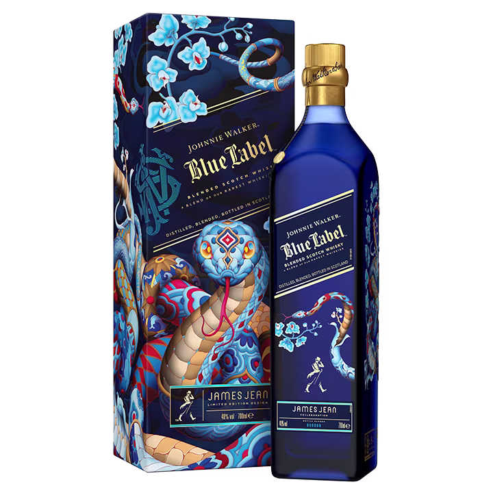Een blauwe fles Johnnie Walker Blue Label whisky staat naast een uitgebreide doos met kleurrijke, artistieke ontwerpen van een slang en bloemen. De doos toont de naam James Jean en past bij het etiket van de fles met gouden accenten.