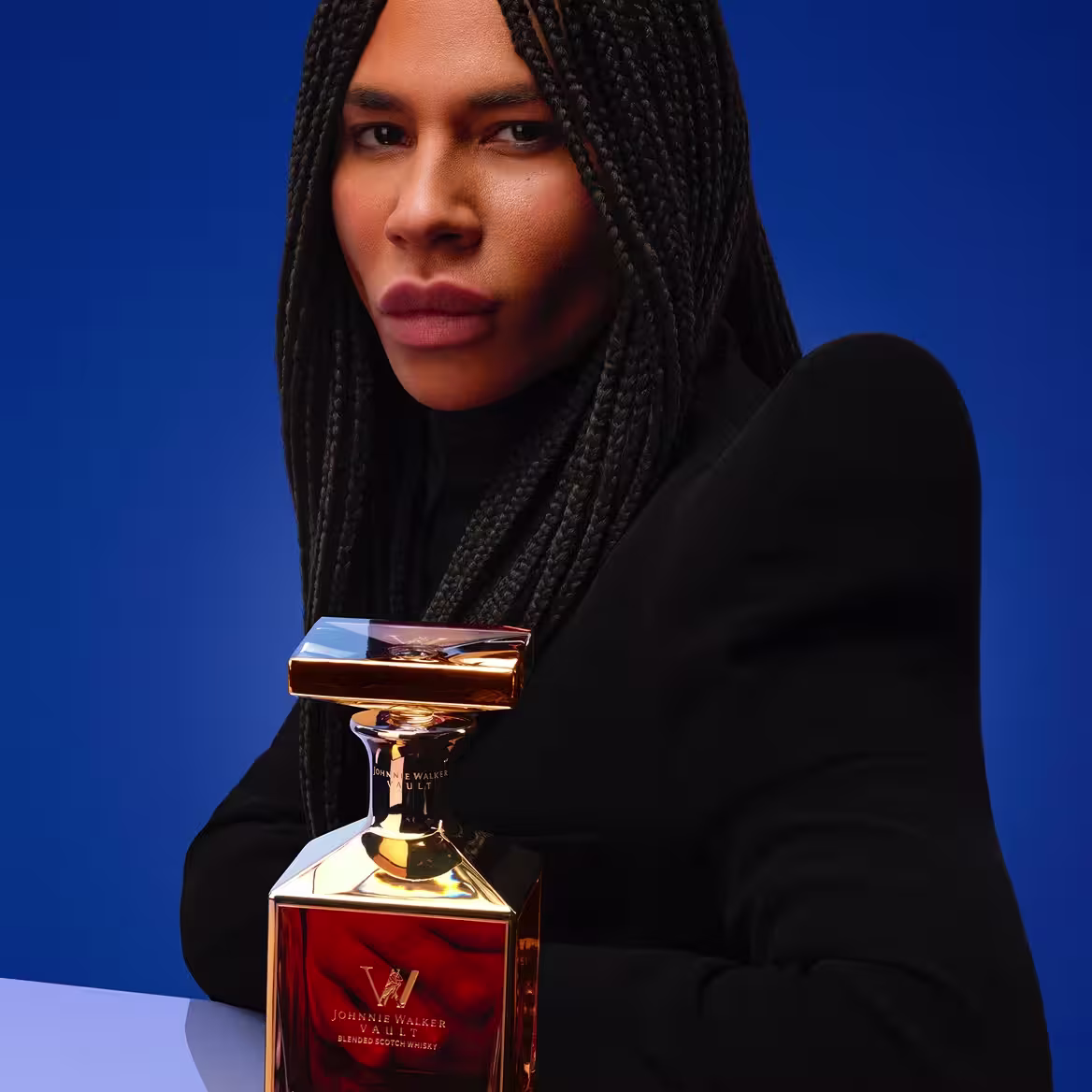 A woman with braided hair wearing dark clothing stretches her hands toward the camera, creating a dramatic, close-up perspective. The background is blurred and bright, emphasizing her hands and face.