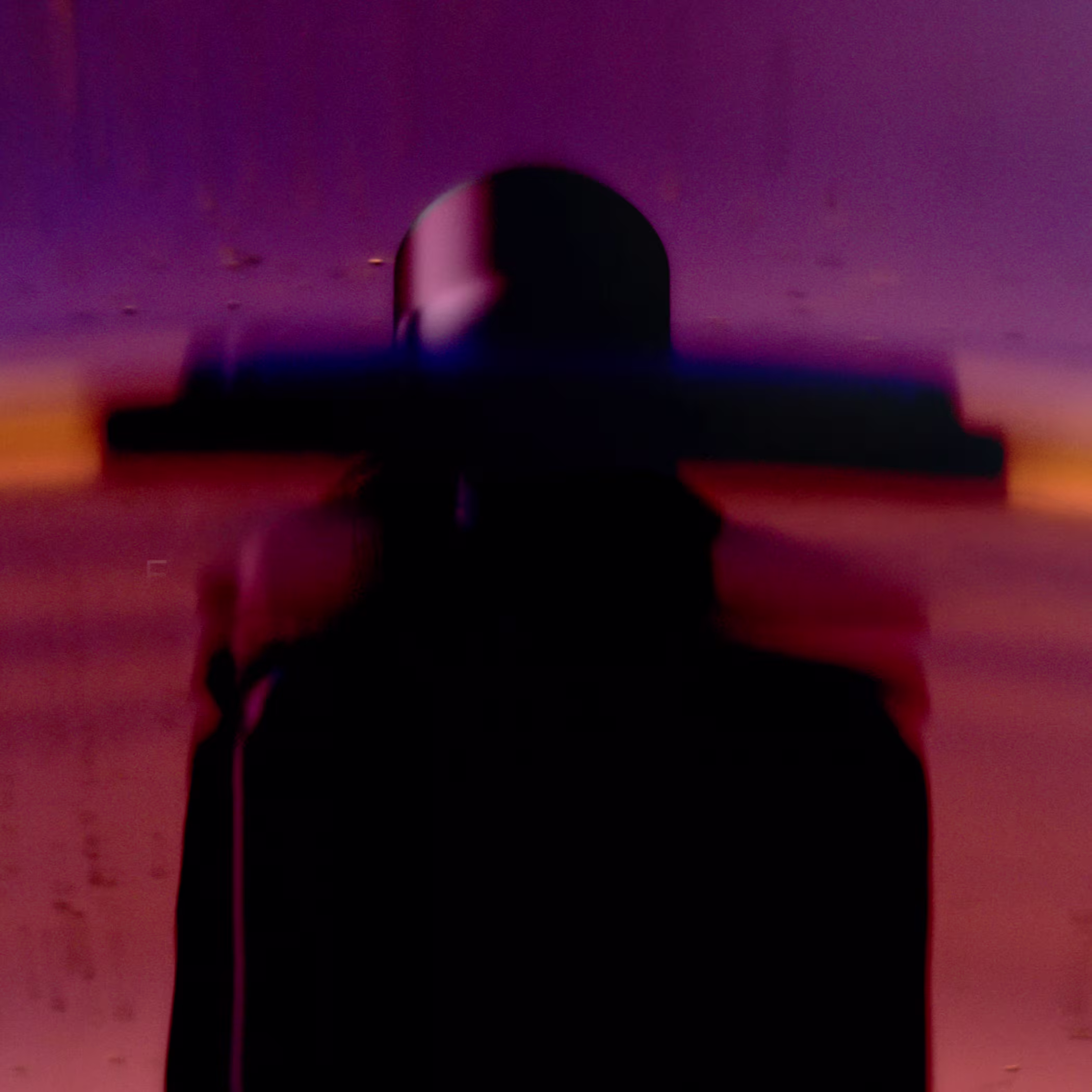 Blurred silhouette of a figure in a wide-brimmed hat against a purple and orange background.