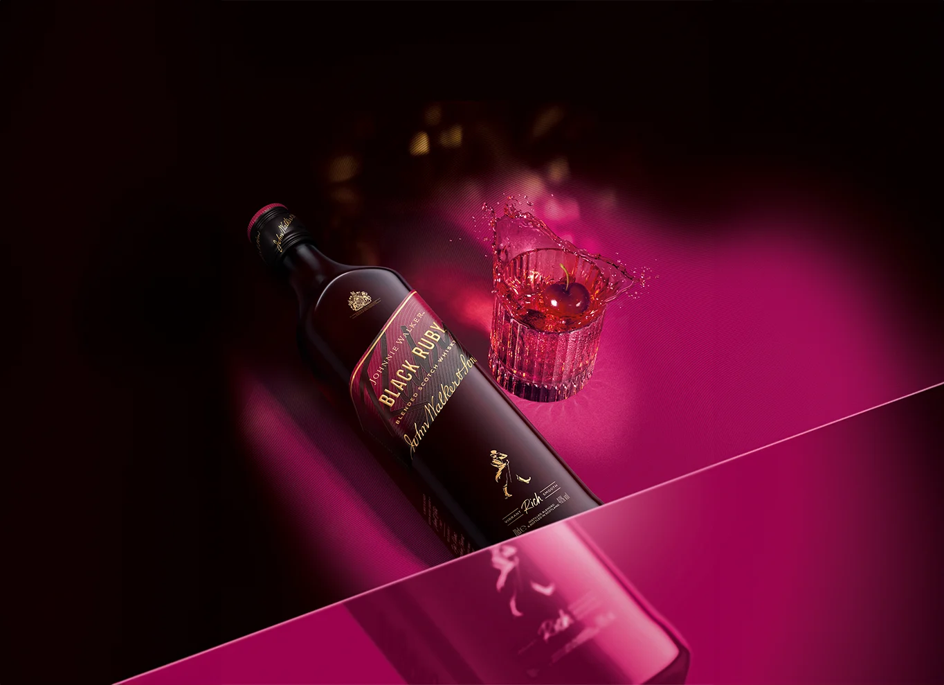 Een fles Black Ruby whiskey ligt op een roze ondergrond naast een glas gevuld met een spetterende rode drank. De fles en het glas worden uitgelicht tegen een donkere achtergrond, wat een dramatisch effect creëert.