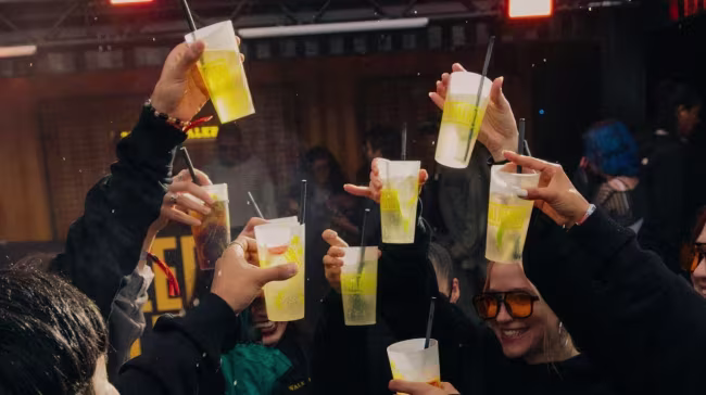 Eine Gruppe von Menschen auf einer Party, die Plastikbecher mit Trinkhalmen zum Anstoßen in die Höhe hält.