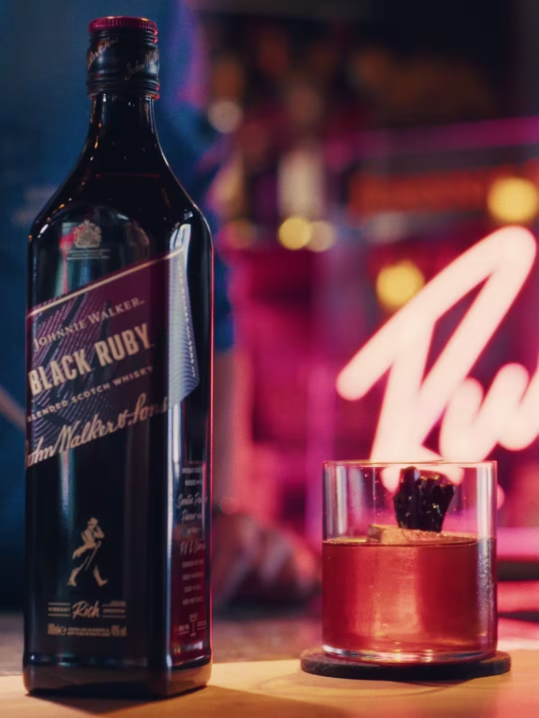 Een barman in een groenblauw jasje schenkt een drankje in een beker achter de bar, terwijl een klant met een beige pet toekijkt vanaf de andere kant van de toonbank.