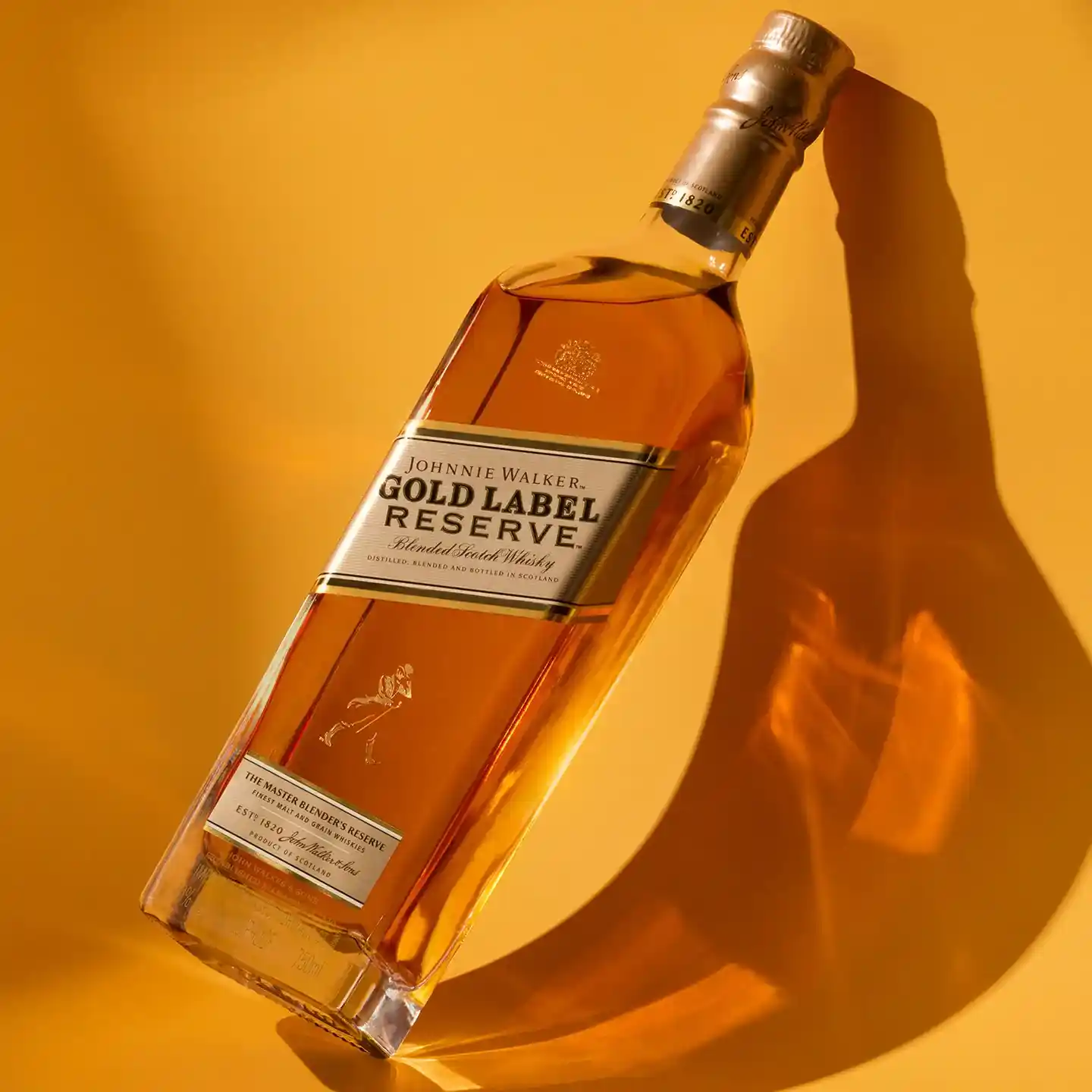 Na žlutém povrchu stojí láhev Johnnie Walker Gold Label Reserve Blended Scotch Whisky