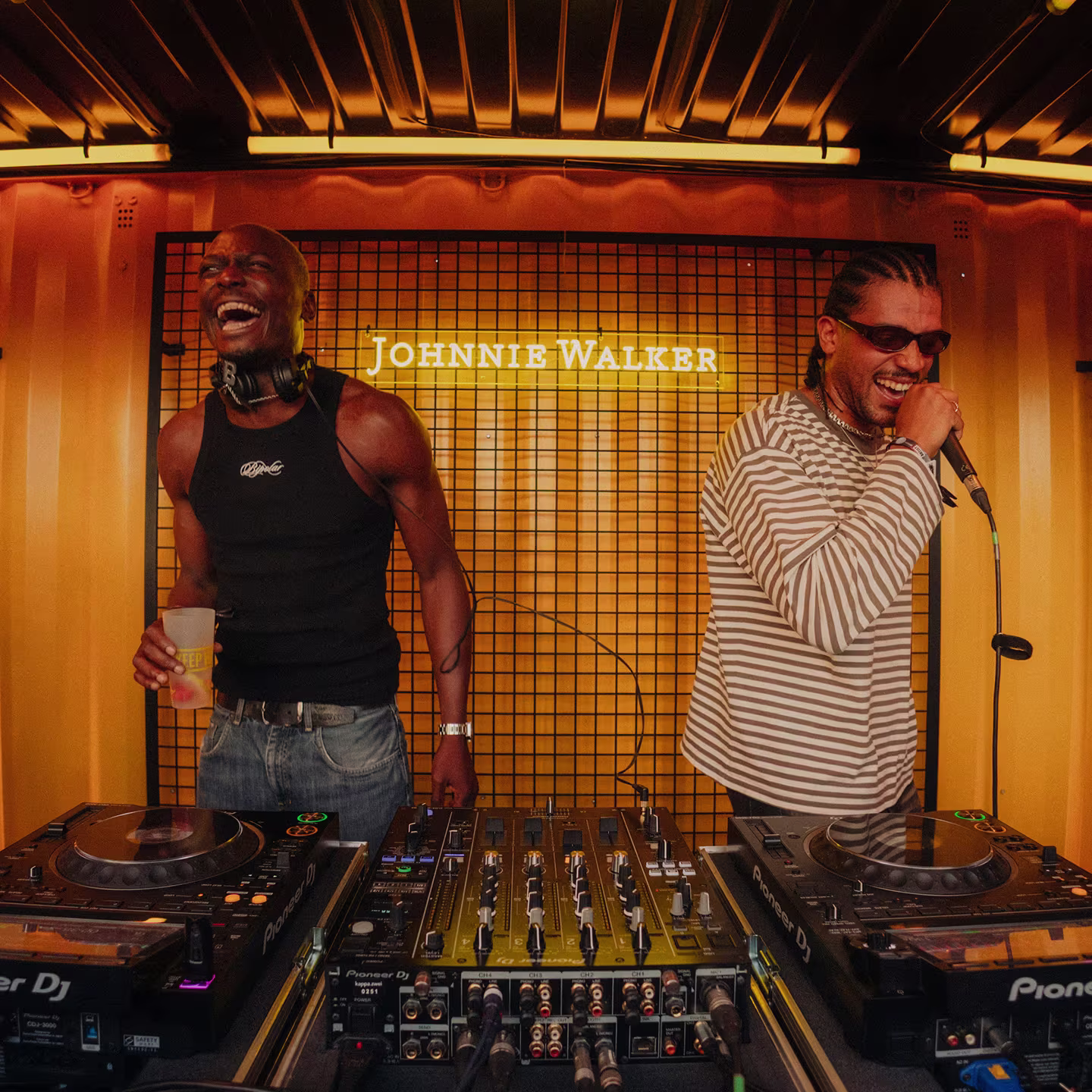 Zwei DJs lachen hinter dem Mischpult auf einer Johnnie Walker Bühne.