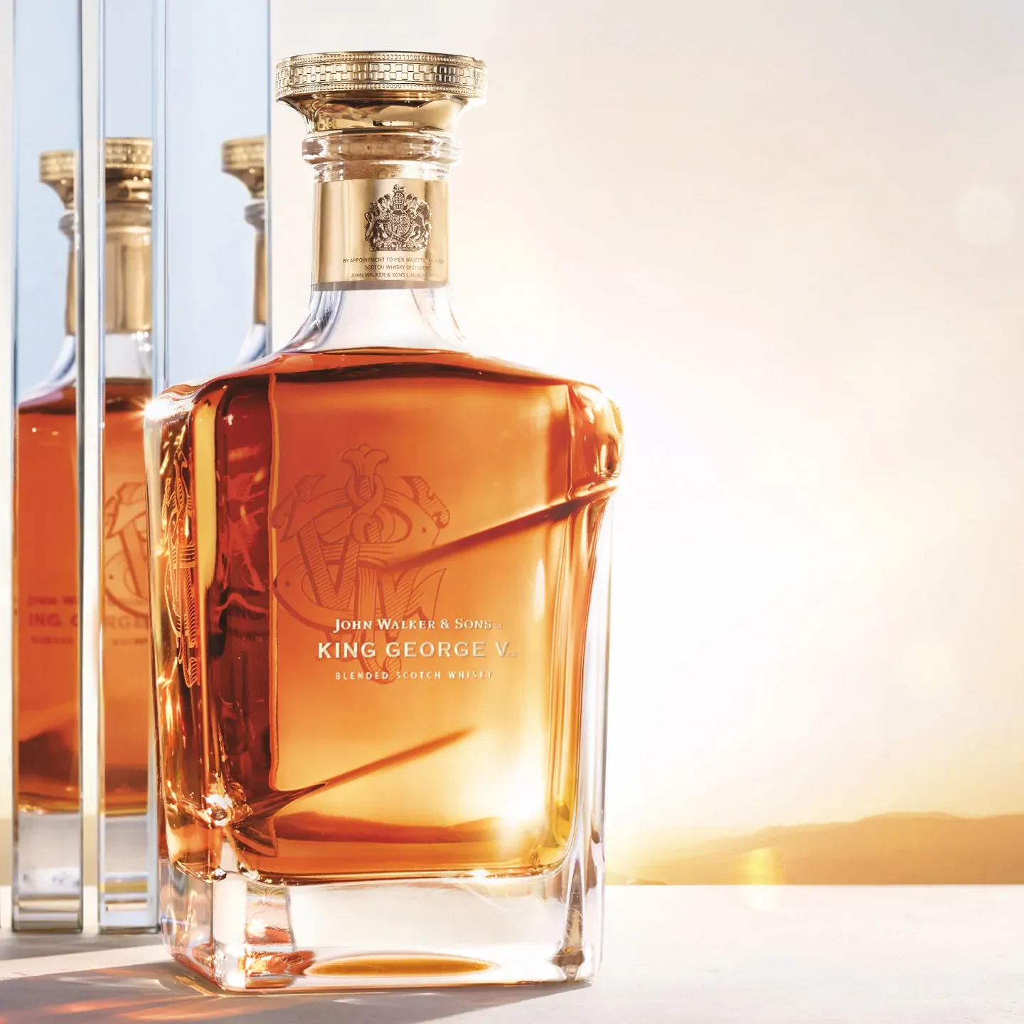 Eine Flasche John Walker & Sons King George V Blended Scotch Whiskey mit einer goldenen Flüssigkeit im Inneren steht auf einer reflektierenden Oberfläche. Die elegante Flasche weist komplizierte Designdetails auf und steht vor einem warmen Hintergrund.