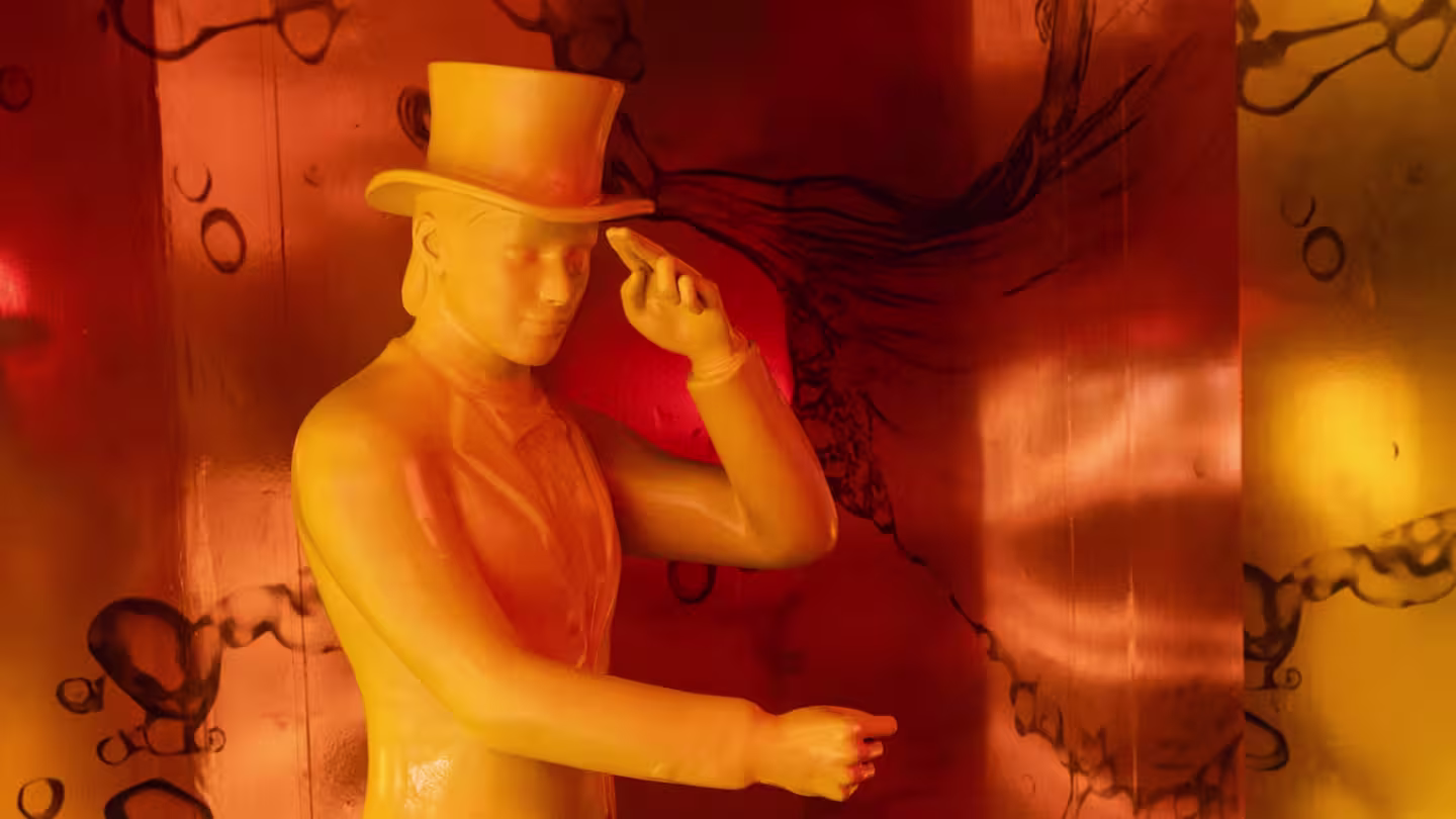 Una estatua amarilla de una persona con sombrero de copa y traje se inclina el sombrero. El fondo es naranja con patrones abstractos y diseños circulares.