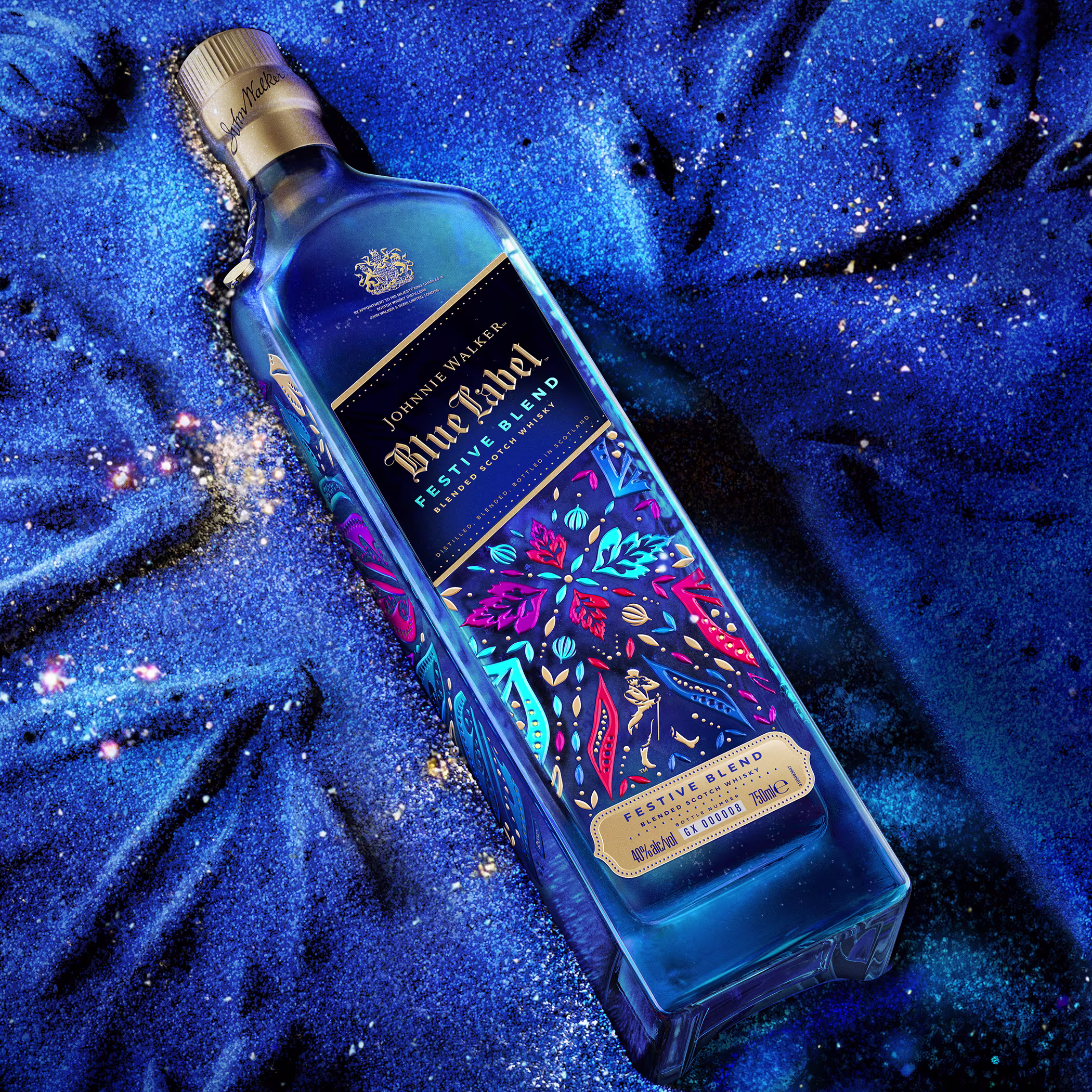 Johnnie Walker Blue Label Festive Blend bottle lying on a deep blue, sparkling textured surface.