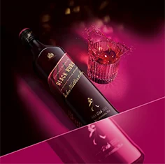 Una botella de whisky escocés mezclado Johnnie Walker Black Ruby sobre un fondo rosa oscuro. La etiqueta es negra con un detalle rosa y lleva el texto Black Ruby y detalles de la marca. La botella se encuentra inclinada sobre una superficie negra.