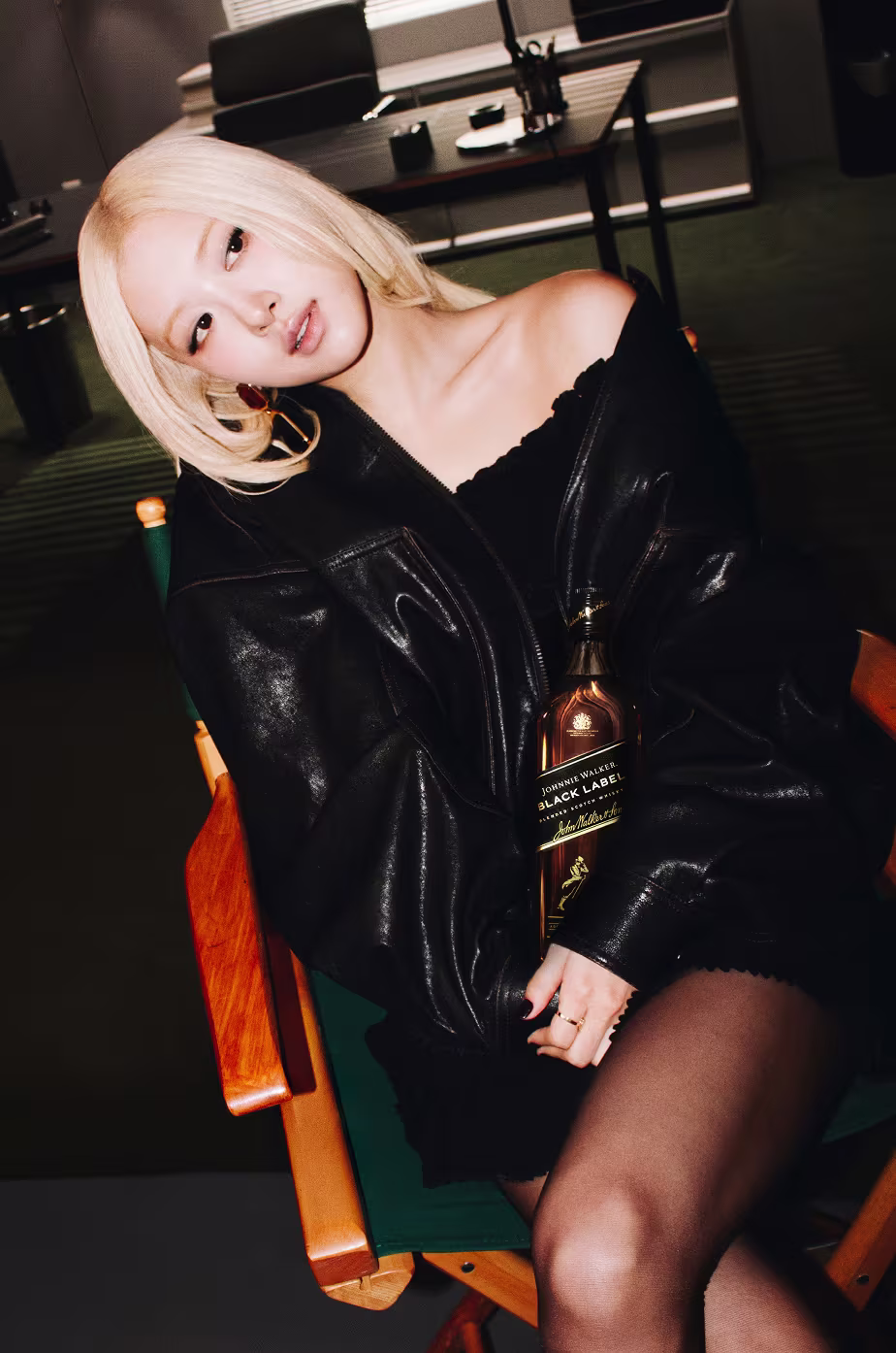 ROSÉ in a black leather jacket sitting in a director's chair, holding a bottle of Johnnie Walker Black Label.