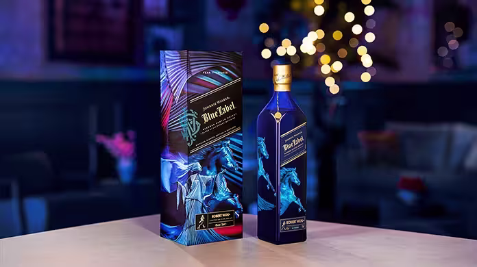 ขวดสีน้ำเงินของ Johnnie Walker Blue Label Year of the Horse พร้อมกล่องตกแต่งที่เข้าชุดกันซึ่งมีภาพศิลปะม้าสีน้ำเงิน วางอยู่บนโต๊ะที่มีพื้นหลังเบลอ