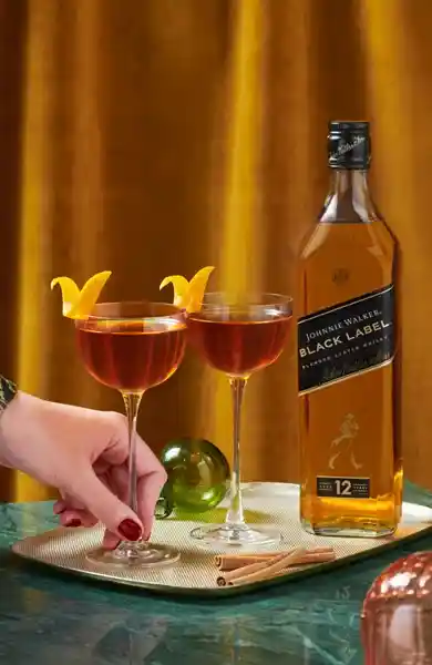 Two cocktails with orange peels and a bottle of Johnnie Walker Black Label whiskey. 
