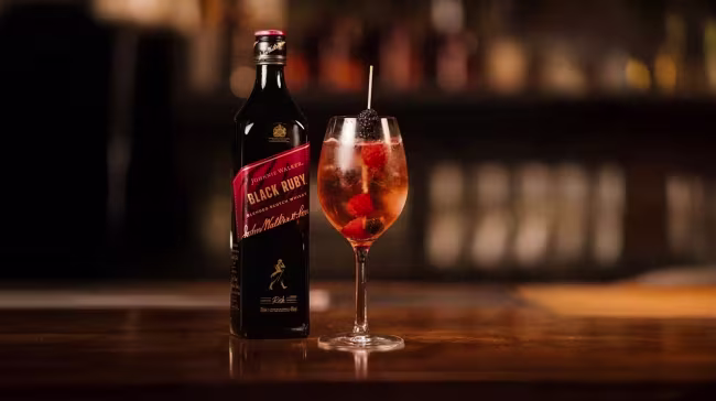 Eine Flasche Johnnie Walker Black Ruby und ein mit Beeren garnierter Cocktail in einem Weinglas.