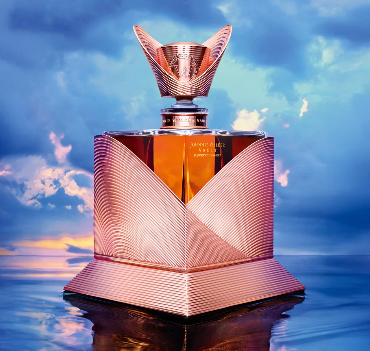 A luxurious, ornate bottle of Johnnie Walker whisky with copper-toned, sculpted detailing, set against a dreamy sky and reflective water background.