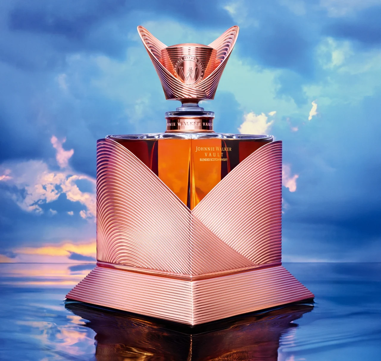 A luxurious bottle of Johnnie Walker Blue Label whisky with an ornate copper and glass design sits on a reflective surface, set against a dramatic sky with soft clouds and warm sunlight.