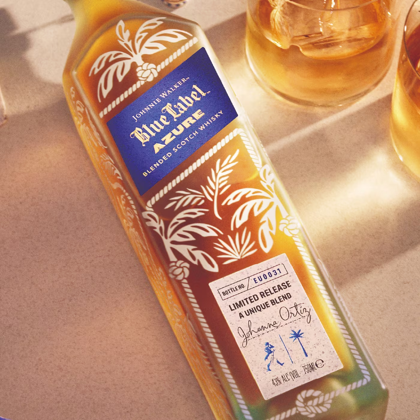 A bottle of Johnnie Walker Blue Label Azure whisky on a light surface beside two glasses of whisky.