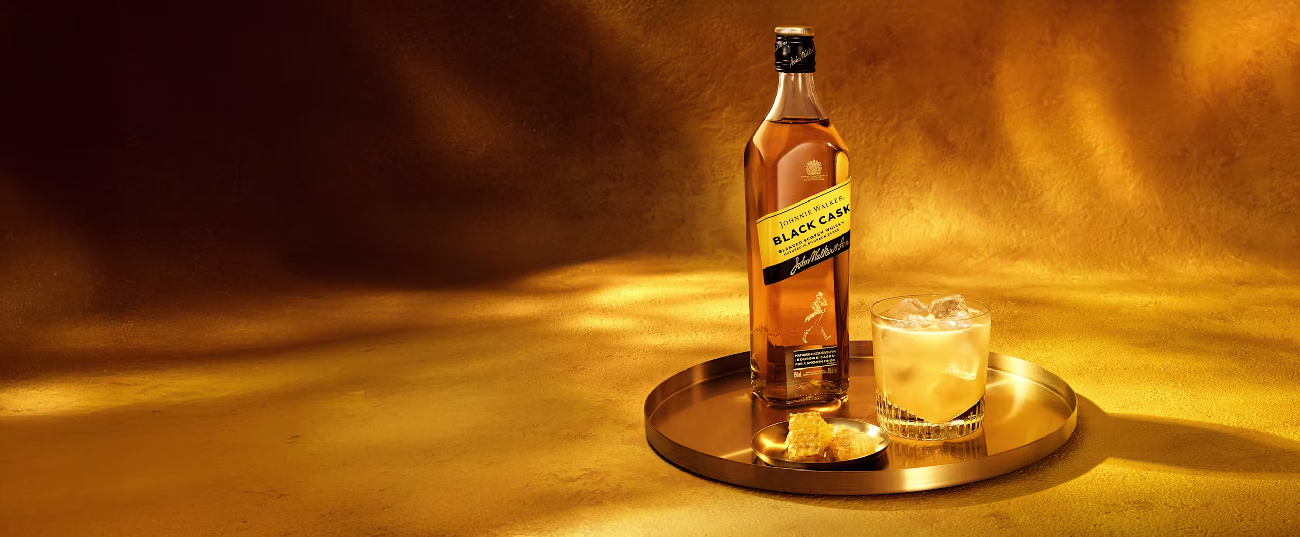 A bottle of Johnnie Walker Black Label and a glass of whiskey on a gold tray with a warm, golden background.