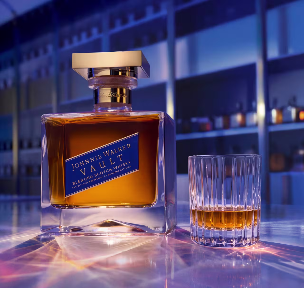 A bottle of Johnnie Walker Vault Blended Scotch Whisky on a softly lit blue bar, with rows of bottles on shelves behind.