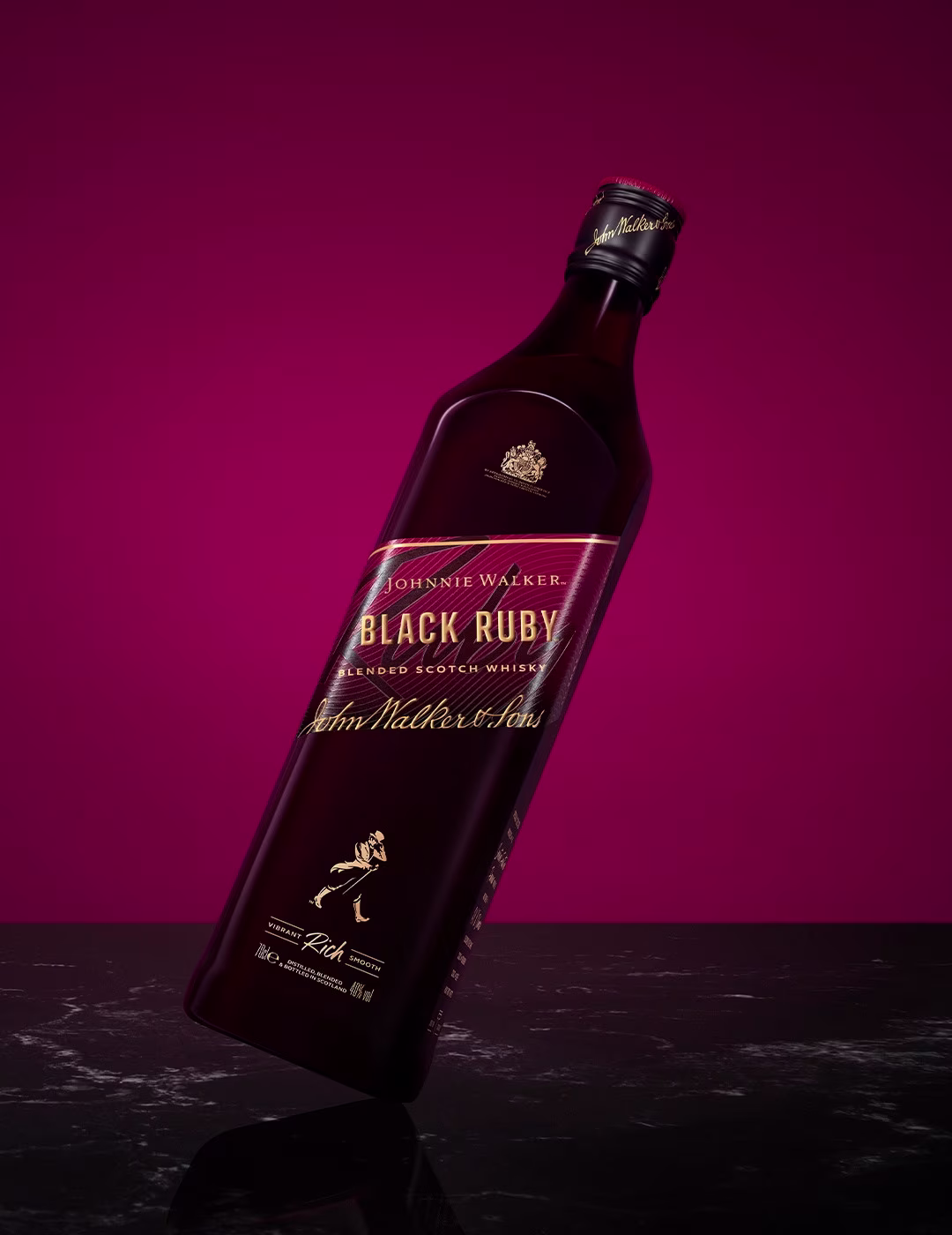 Ένα γερμένο μπουκάλι Johnnie Walker Black Ruby σε ένα πλούσιο μπορντό φόντο. Το μπουκάλι έχει χρυσά γράμματα και το εμβληματικό λογότυπο του striding man. Στηρίζεται σε μια ανακλαστική σκοτεινή επιφάνεια.