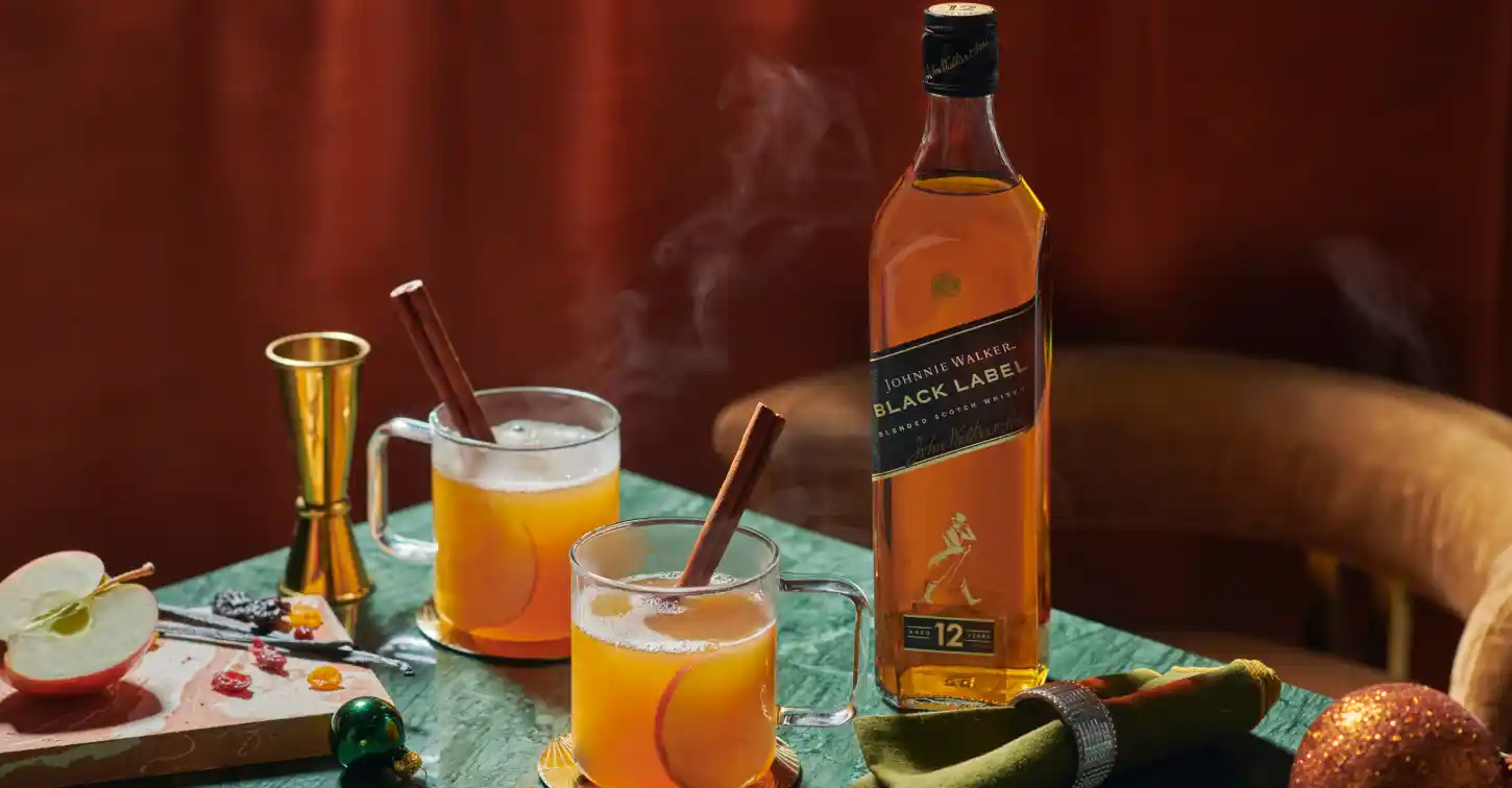 Dva páry horké jablečné šťávy s párou a láhev Johnnie Walker Black Label whiskey.