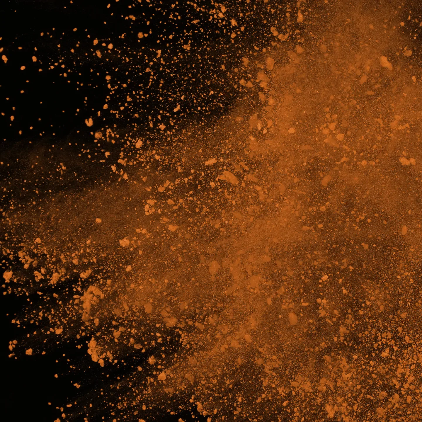  Orange powder dynamically disperses on a black background. It creates bright and textured abstract patterns.