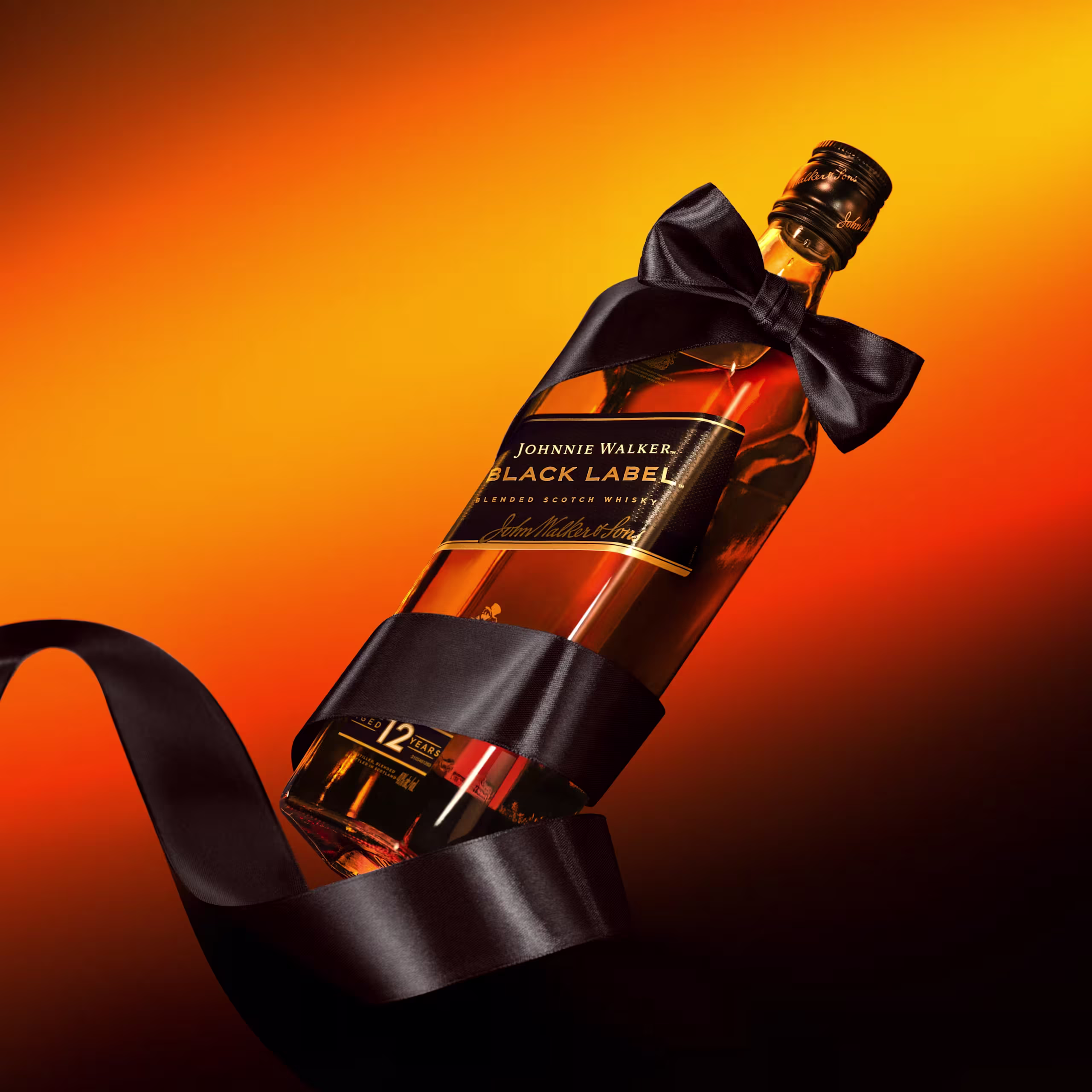 Een fles Johnnie Walker Black Label whisky met een zwarte strik om de hals en lint, tegen een levendige oranje en gele achtergrond.